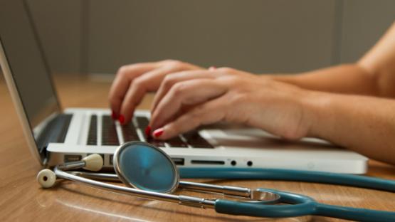 Person sitting while using laptop computer and green stethoscope near