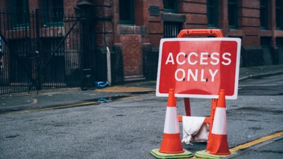 Red street sign saying Access Only on empty city road with two traffic cones