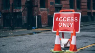 Red street sign saying Access Only on empty city road with two traffic cones
