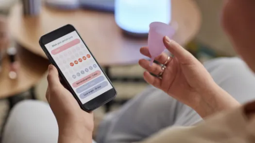 Someone holding a menstrual cup and looking a generic period tracking app
